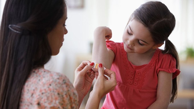 an adult opening a bandaid to put on a girl's elbow