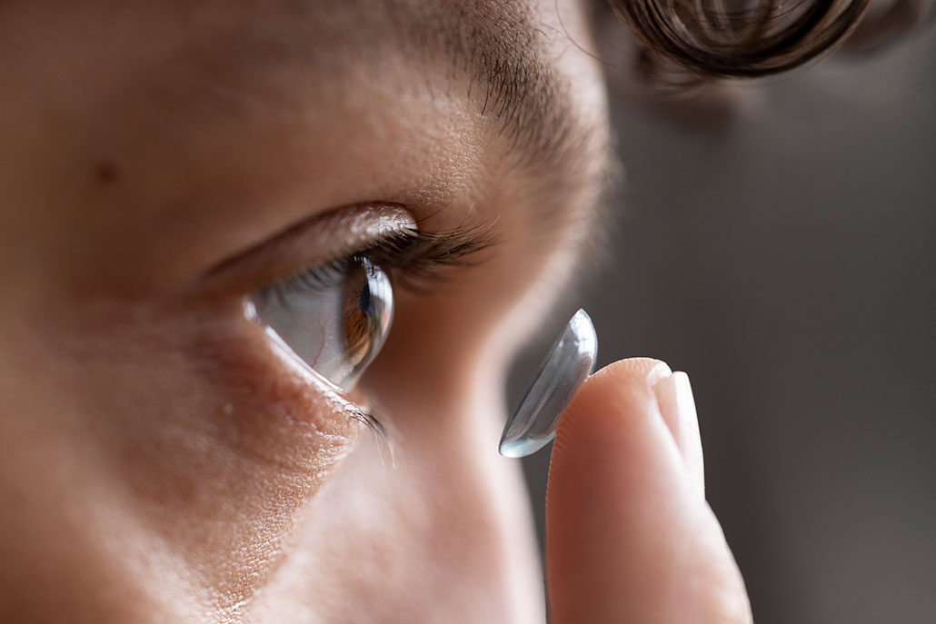 a side-view close-up of a person bringing a contact on their finger close to their eye before inserting it
