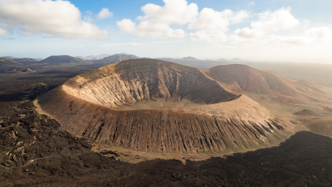 a mountain with a caldera, a huge bowl-shaped crater in the center, sits under a blue sky