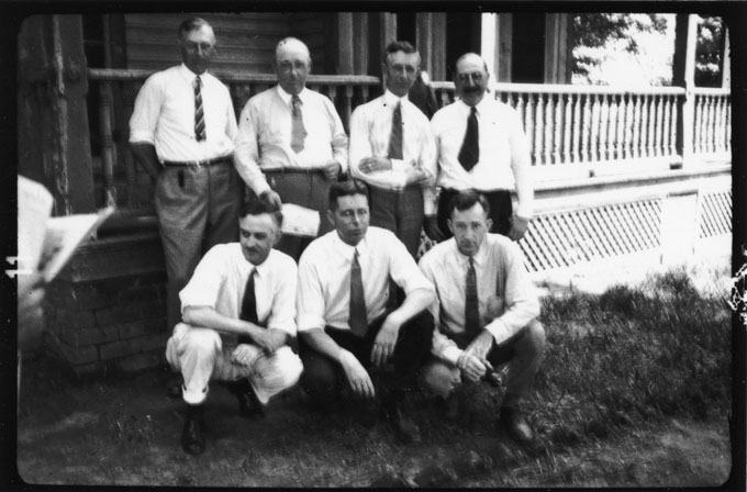A photo of seven people posing for a portrait in front of a porch.
