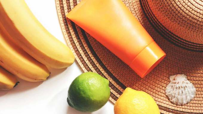 a tube of sunscreen, a wide-brimmed hat, bananas, a lime, a lemon, and a seashell