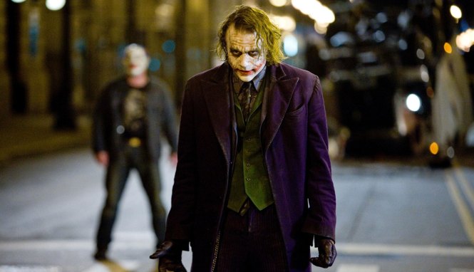 a movie still from the Joker movie where villain the Joker is standing on a street and staring someone down
