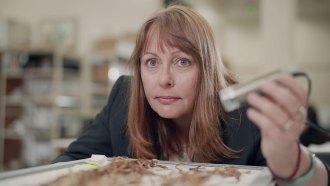 A researcher is shown holding a device over a tray of strings, an example of an Inca recordkeeping device called a khipu.