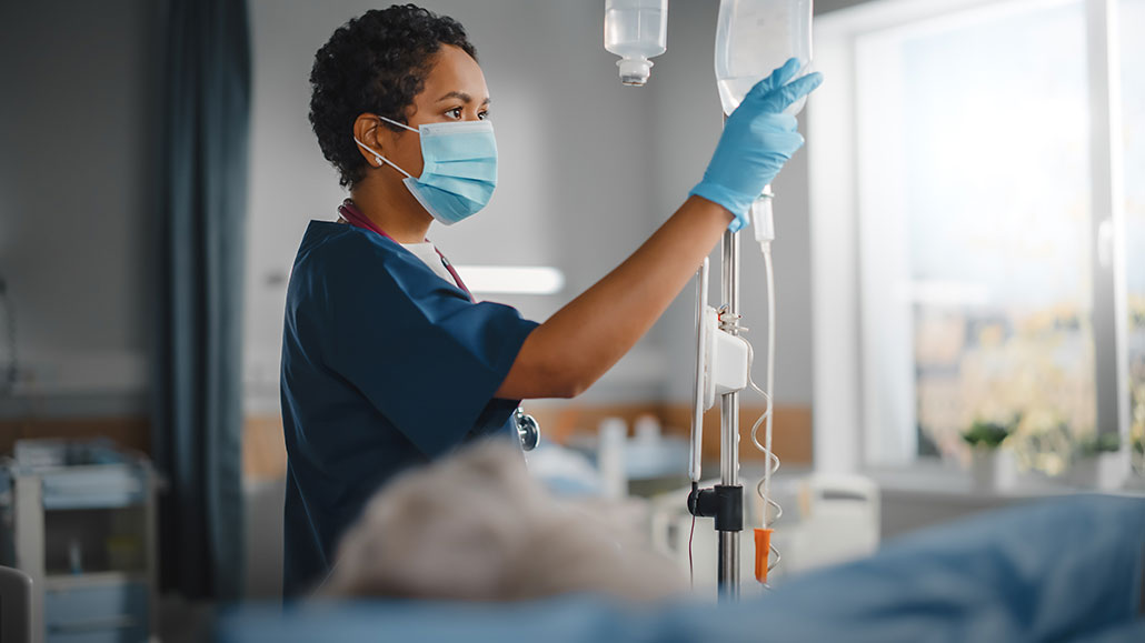 a medical worker wearing a surgical mask and sterile gloves checks on an IV bag filled with liquid