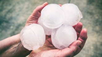 two hands holding several baseball-sized balls of hail