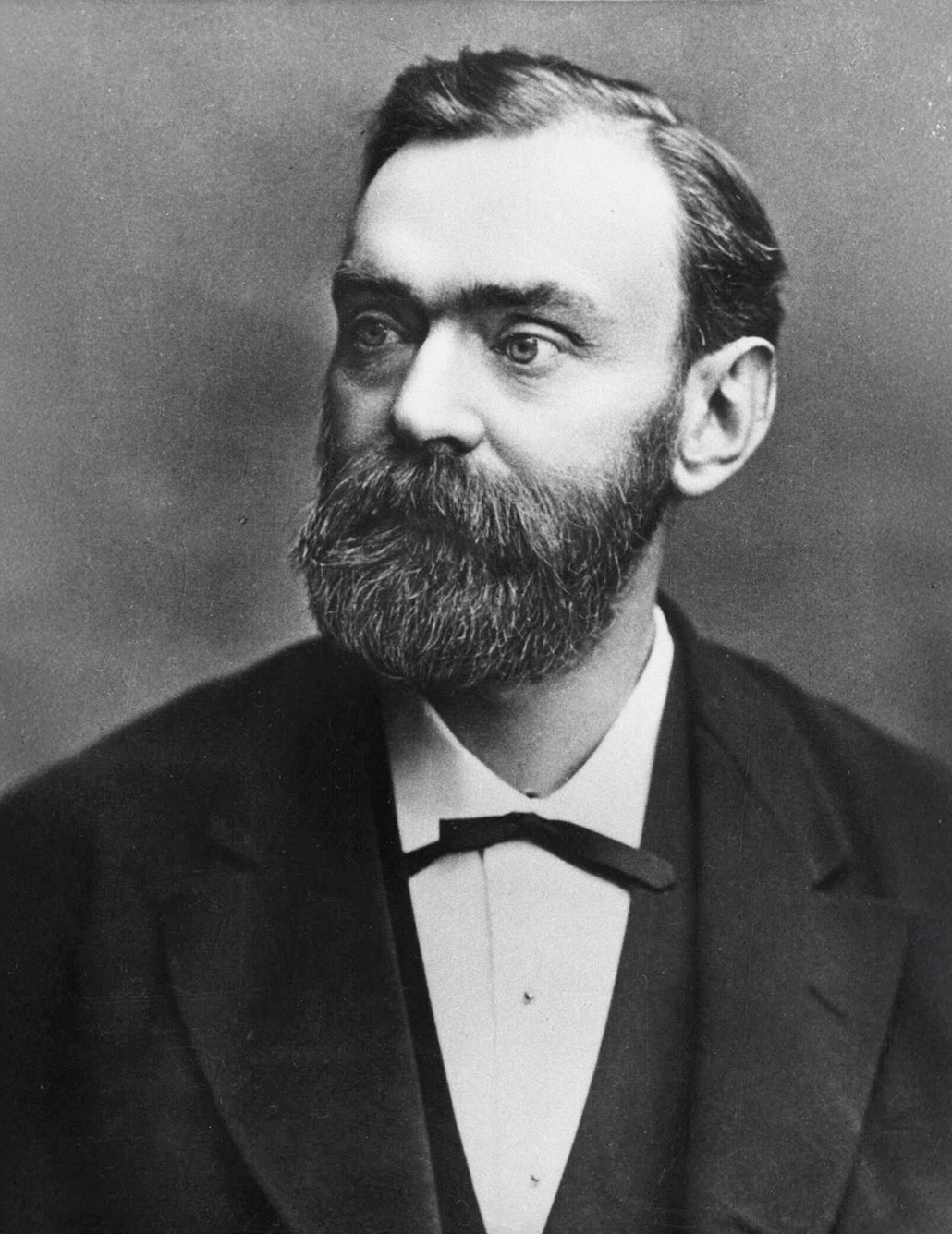 a black and white photo of a man with pale skin, short hair, a bushy beard and mustache wearing a suit