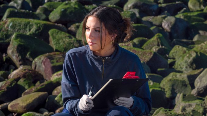 Shark researcher Heidy Martinez stands in front of a rocky coast.
