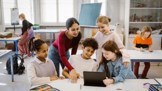 a teacher leans over a table where students are working together happily
