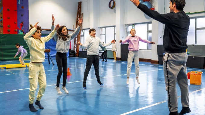 a group of middle school kids doing jumping jacks in a gym as directed by their teacher
