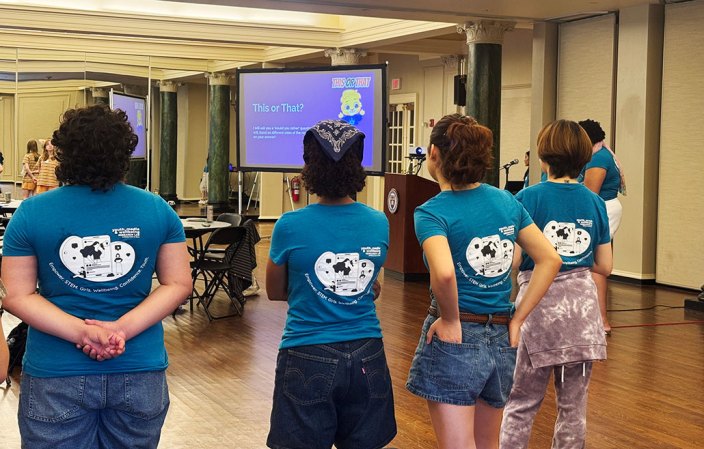mentors wearing blue shirts face away from the camer and towards their teen workshop attendees at an event
