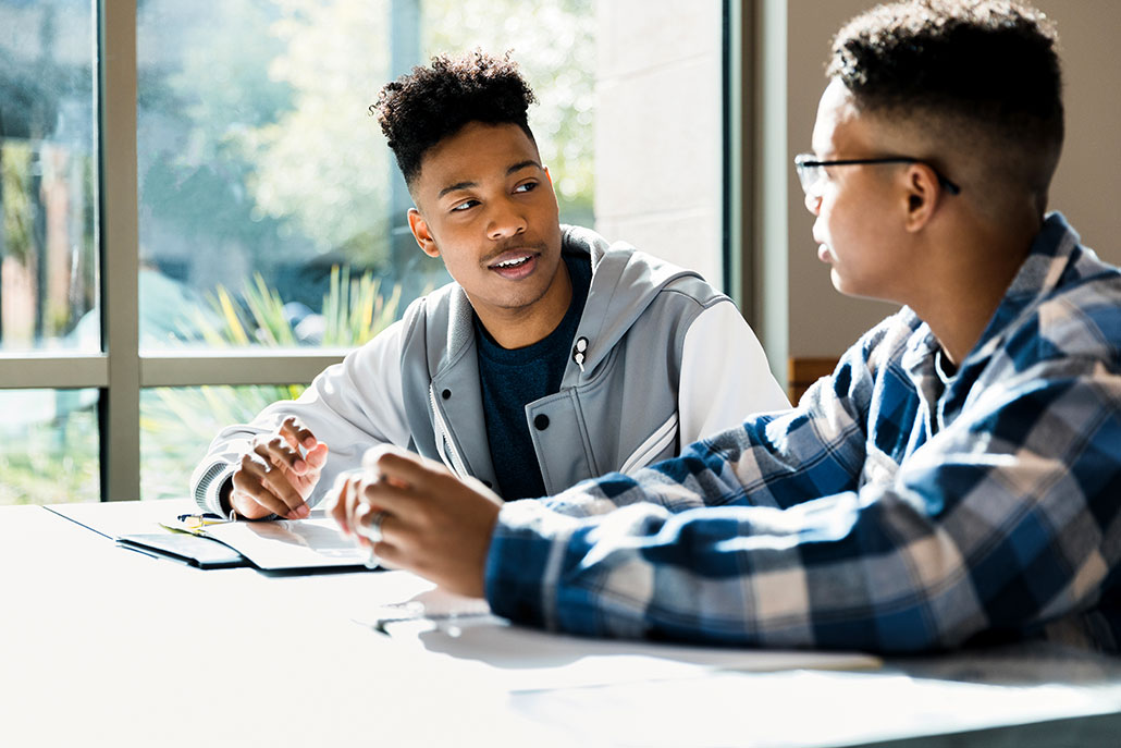 two African American teens sitting at a table and having an earnest conversation