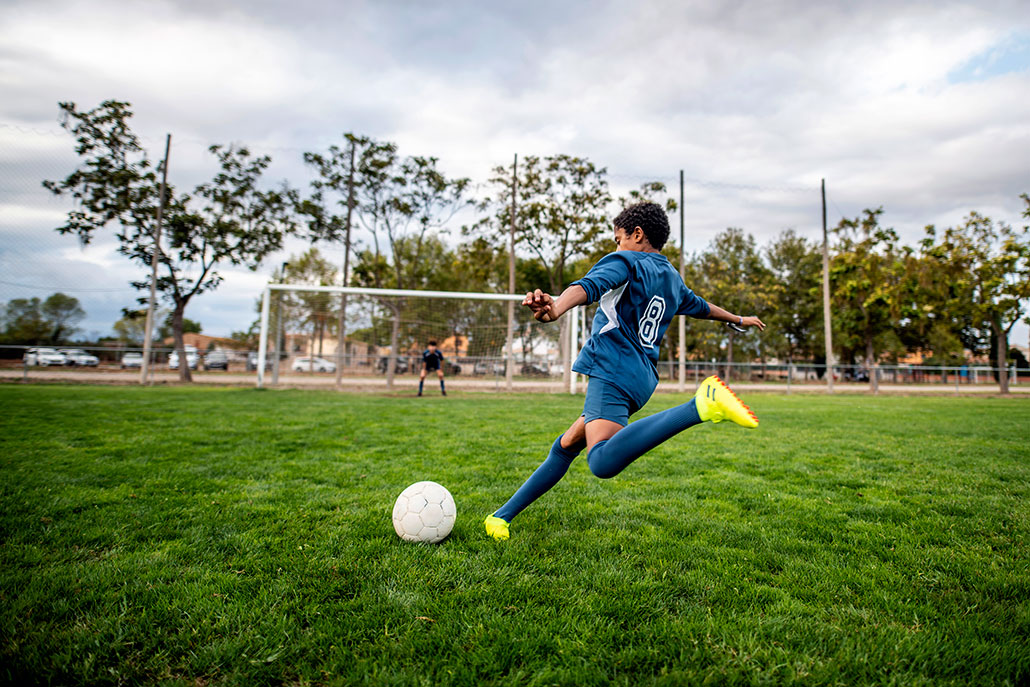 a boy in a blue soccer uniform is about to kick a soccer ball into the goal