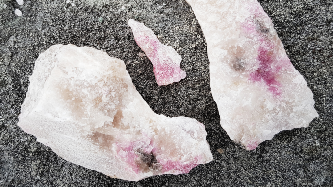 three chunks of milky white rock with tinges of pink are displayed on asphalt