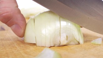 a close up view of a person holding half an onion on a cutting board and using a knife to cut it