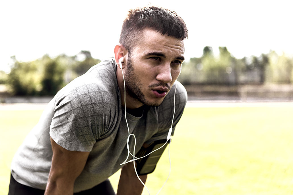 a young man wearing white headphones bending over and exhaling heavily after excercise