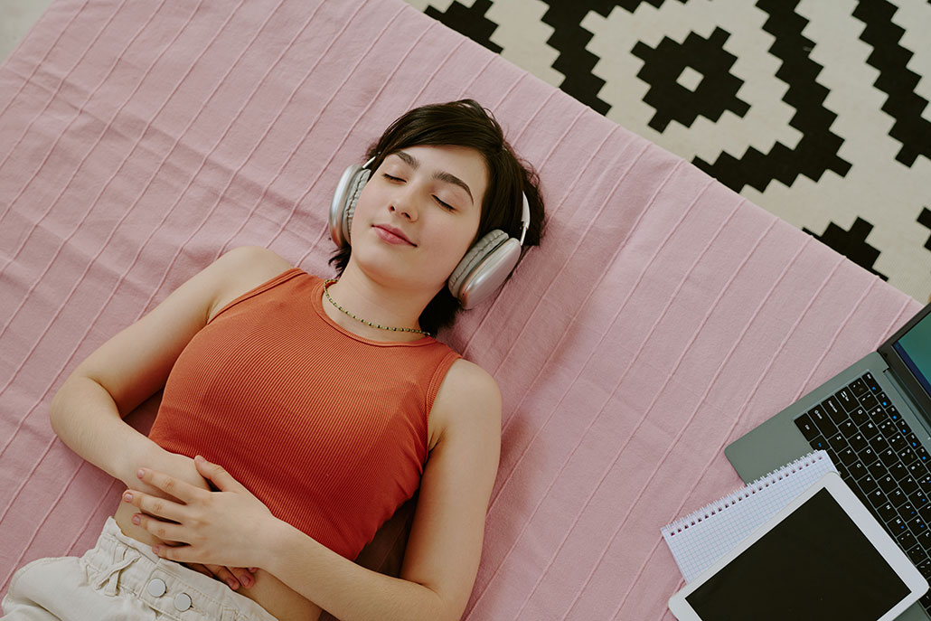 a woman lies on her bed with her eyes closed while listening to something over headphones