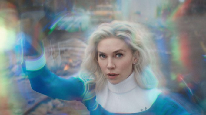 Fantastic Four’s Invisible Woman stands against a warped, kaleidoscopic background. She is a white woman with blue eyes and platinum blonde hair. She is wearing a blue bodysuit with white cuffs and collar.