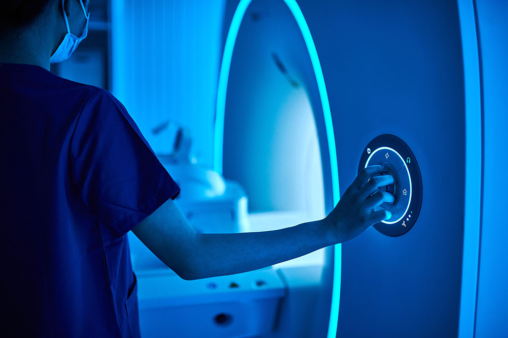 a nurse puts her hand on the controls of a blue glowing MRI machine
