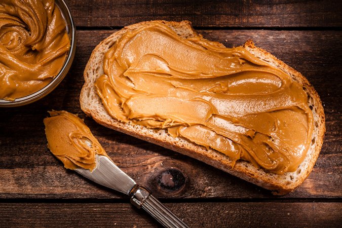 a slice ofbread on a wood surface, peanut butter has been spread on the bread