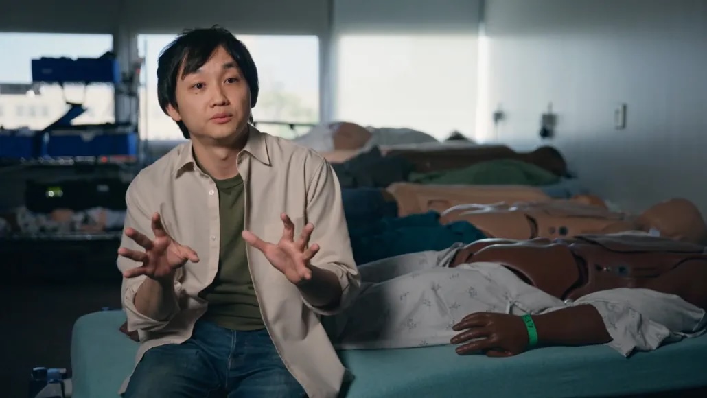 a doctor sits on a bed next to mannequins lying on their stomachs with their bottoms showing