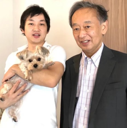 Takanori Takebe stands next to his dad, who inspired his work on butt breathing. He's holding a small dog, and both men smile at the camera.