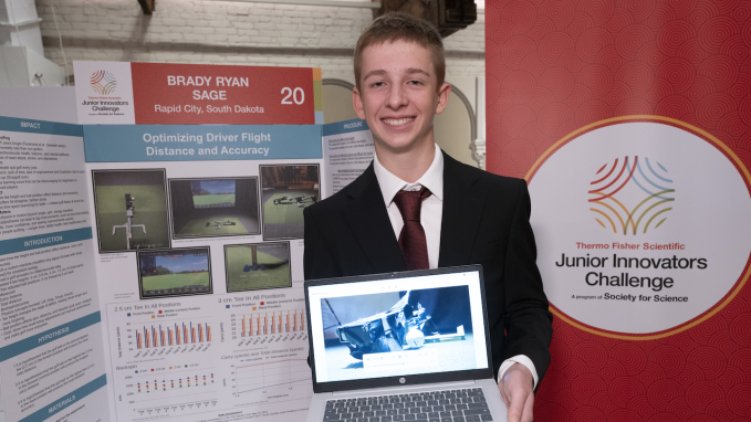 a teen boy smiles as he stands in front of a scientific poster titled "Optimizing Driver Flight Distance and Accuracy"