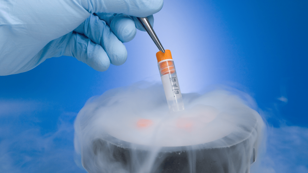 a latex-gloved hand uses tweezers to pluck a phial out of a cup spilling over with dry ice fog