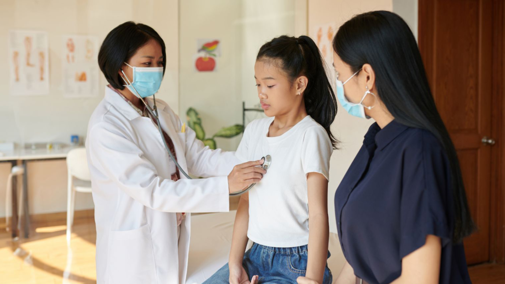 a doctor checks a girls' heartbeat with a stethoscope while her mother watches