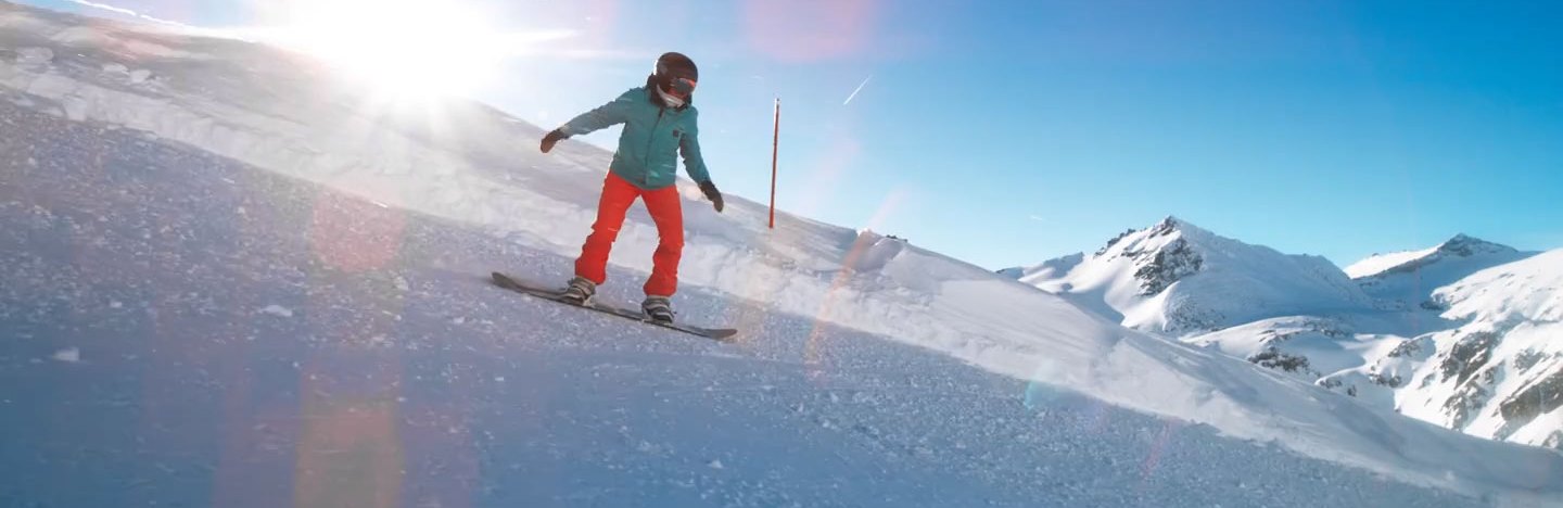 a person snowboarding down a snowy mountain slope with the sun behind them