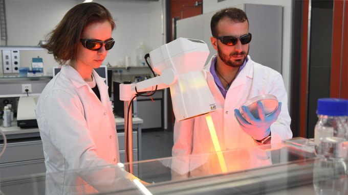 two scientists in white lab coats and dark glasses demonstrating their new graphene-based material that kills germs when activated by light