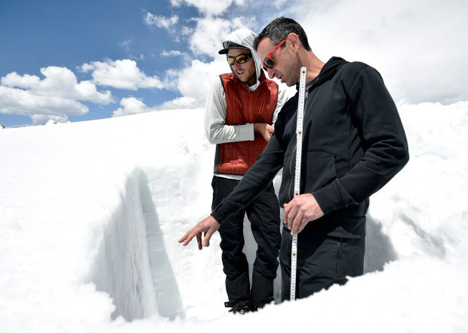 two men stand in a snowbank and measure the snow depth