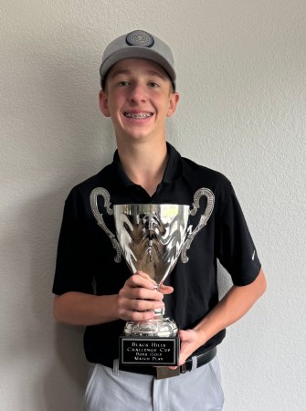 a teen boy smiles as he holds up a golf trophy