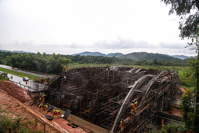 A photo of what looks like a bridge construction over a highway with several builders working on it