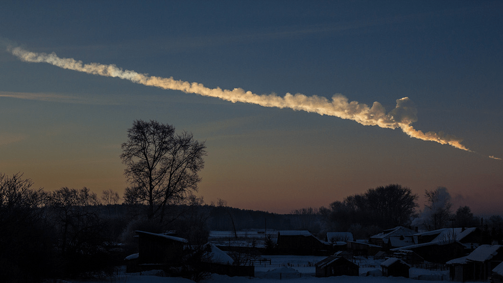the vapor trail of a meteor streaks through a dark blue sky