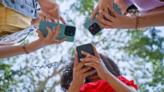 a group of three teens stand in a circle and scroll on their phones as seen from ground up