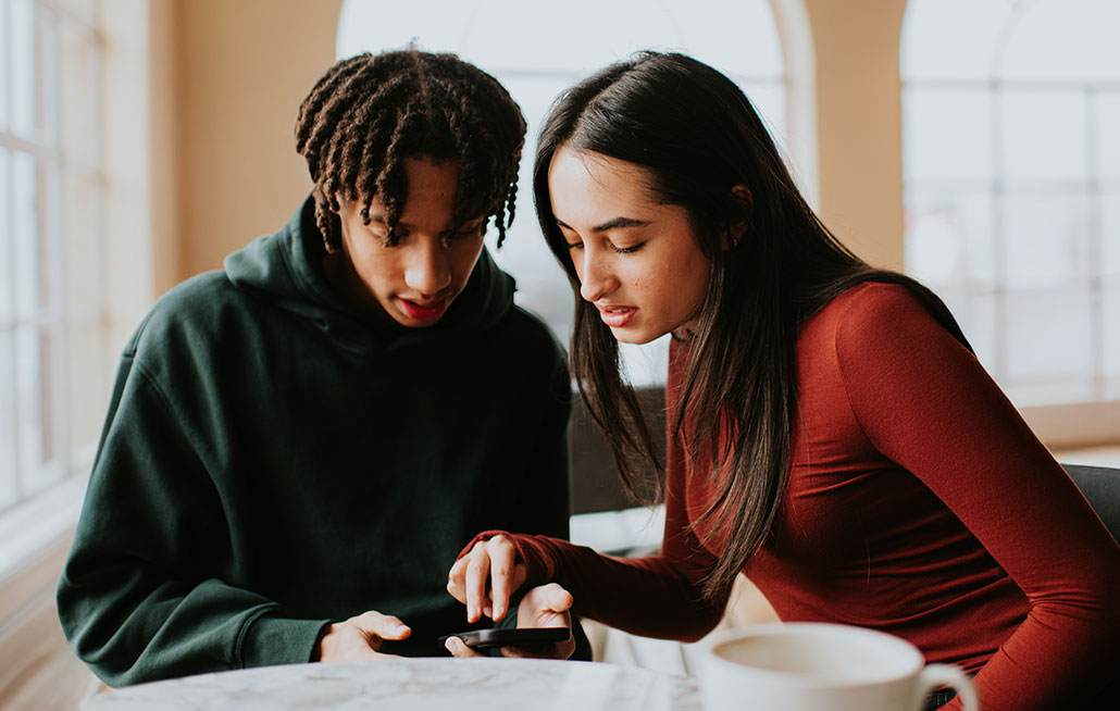 two friends lean over a smartphone in a cafe