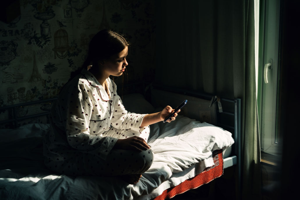 a girl in a low lit room looking stressed, staring at her phone pensively