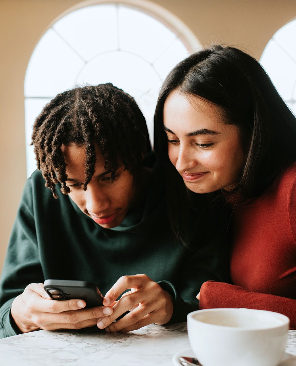 two people look at a phone together at a cafe