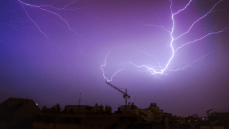 Lightning — a form of electrical discharge — arcs between the sky and a crane on Earth’s surface.