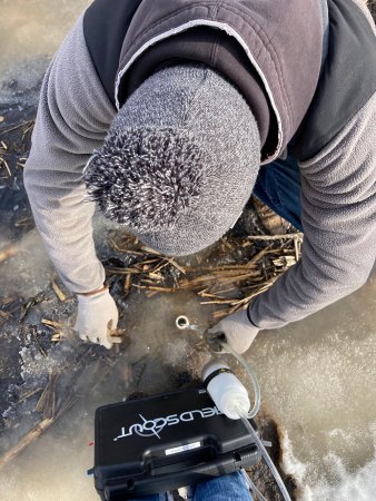 a researcher gets a water sample from the the soil of a field, the researcher is seen from top down bending to get the water sample