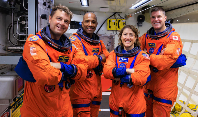 four astronauts stand in orange space suits