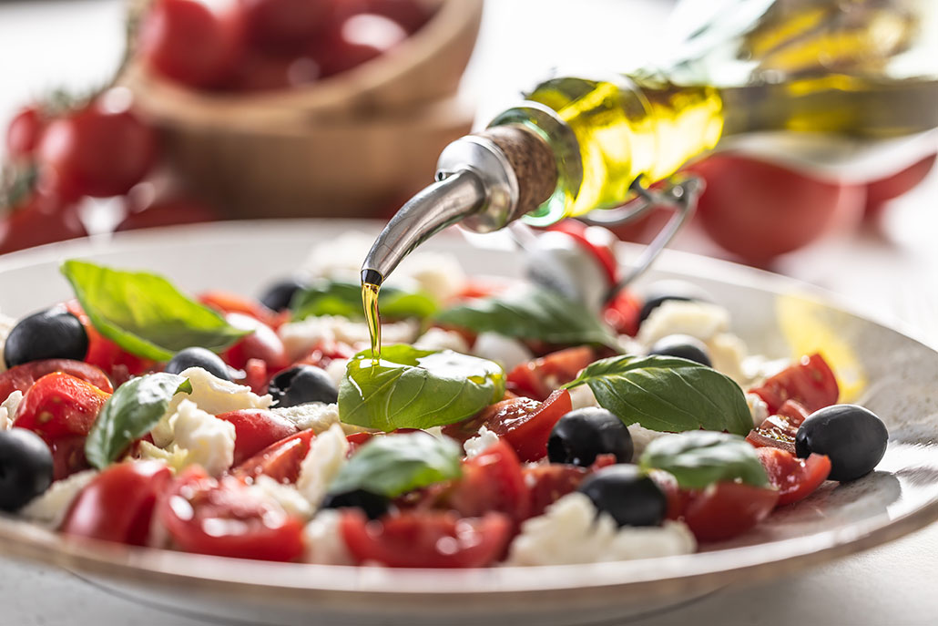 a mozzerella, basil and tomato salad on a plate with olive oil being drizzled on top