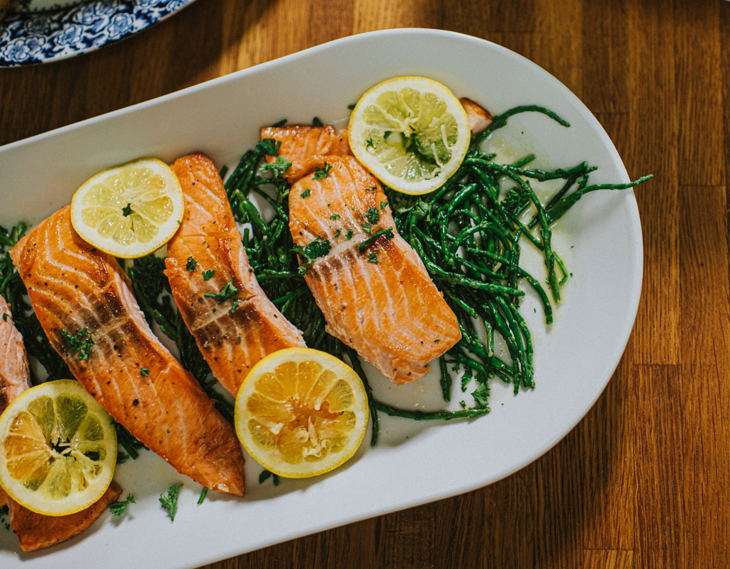 a plate of cooked salmon, greens and lemon slices