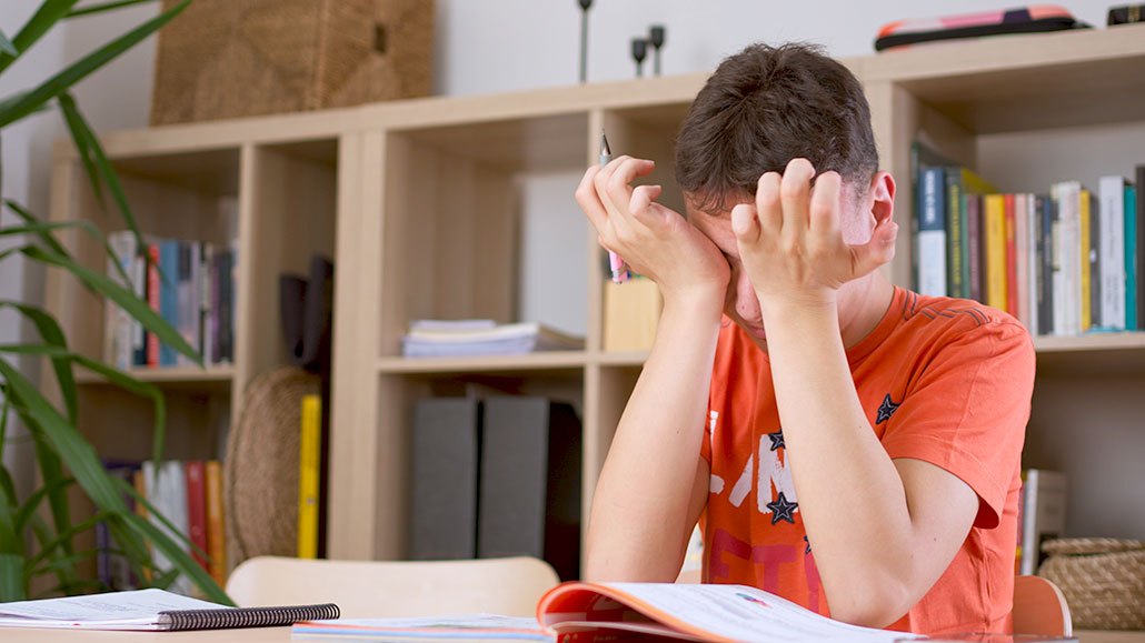 a young teen puts his face in his hands in frustration while studying