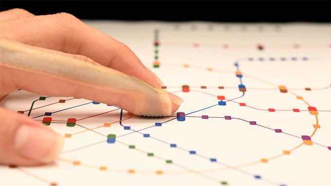 an index finger wearing a band-aid-like device to feel colored dots on a page