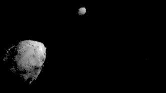 A large grey asteroid looms bottom left on a black background. A smaller space rock hovers at the top center of the image.
