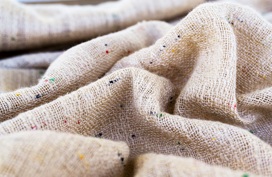 Close-up of loosely woven natural linen fabric with a cream color and small multicolored flecks throughout the weave.