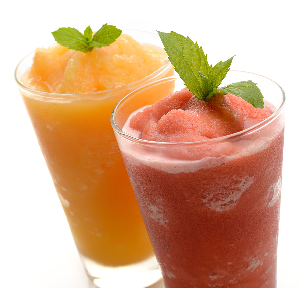 Two fruit slushie drinks garnished with fresh mint leaves — one orange and one pink-red — served in clear glasses against a white background.
