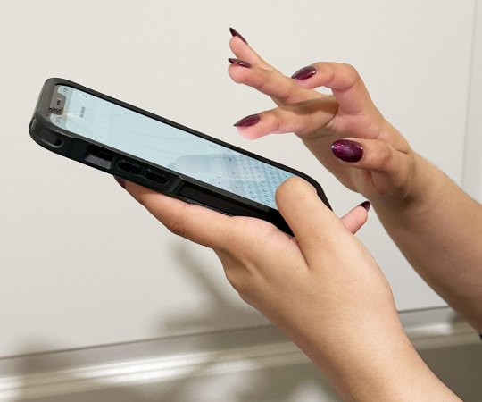 a woman's hands holding a smartphone, because the nails are painted a deep red the user is trying to type with their fingerpads