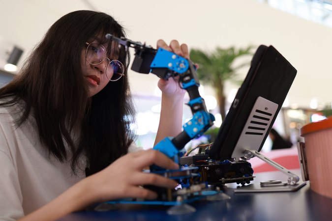 a young woman works with a small robotic arm